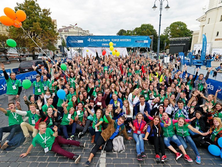Large group of people in green shirts celebrating at an outdoor event with balloons.