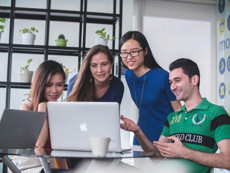 Four people collaborating at a table, looking at a laptop and discussing ideas.