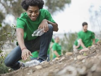 Person in a green shirt crouching down to work on a garden, with others in the background.