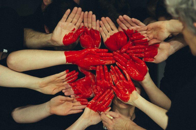 A group of hands with red paint resembling hearts, arranged in a circular pattern.